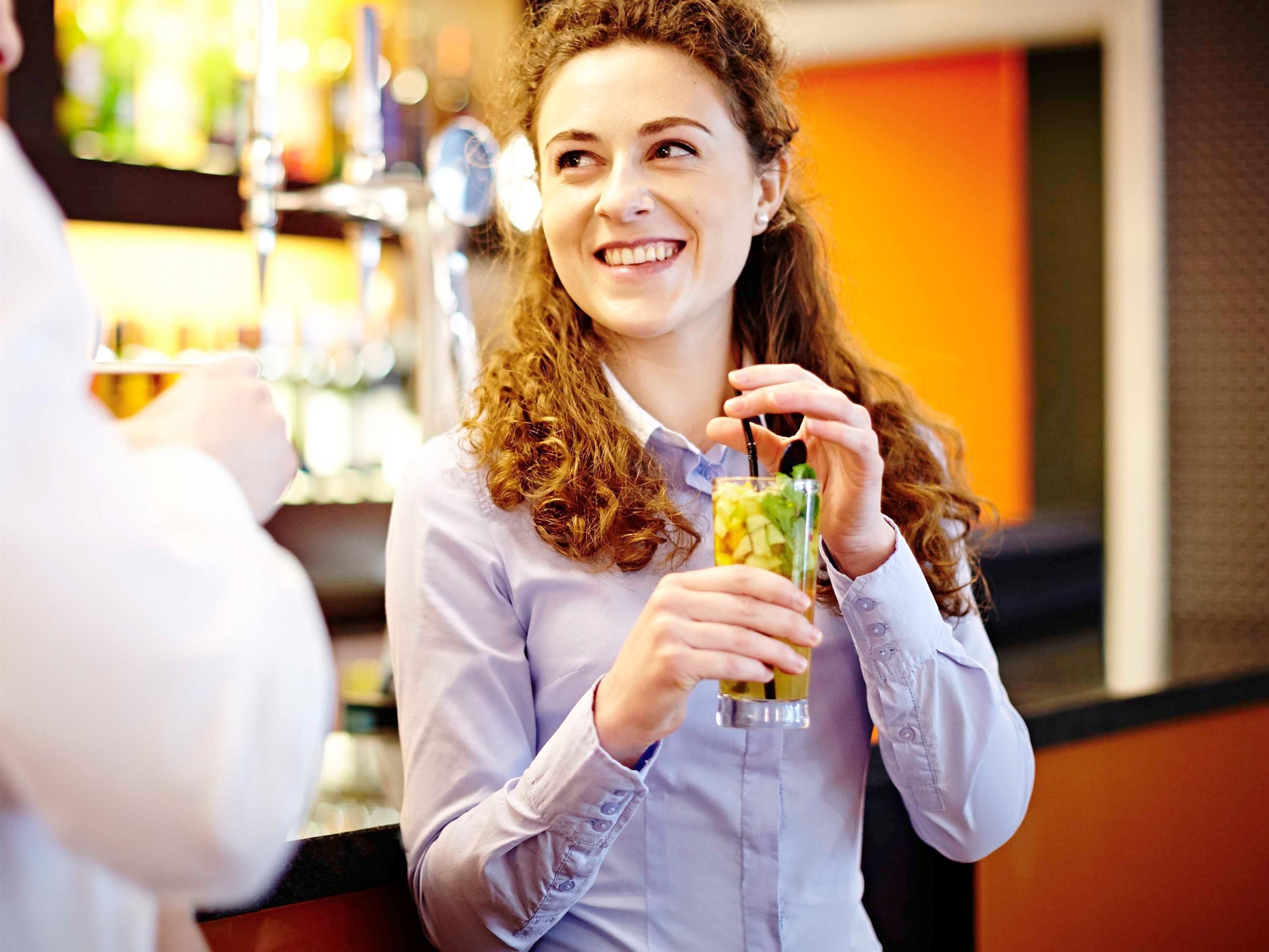 Una persona sosteniendo una bebida en un bar, con estantes al fondo.