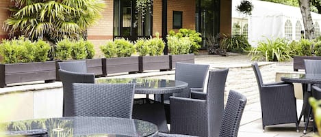 Une terrasse extérieure avec des meubles en osier, un bâtiment en briques et de la verdure.