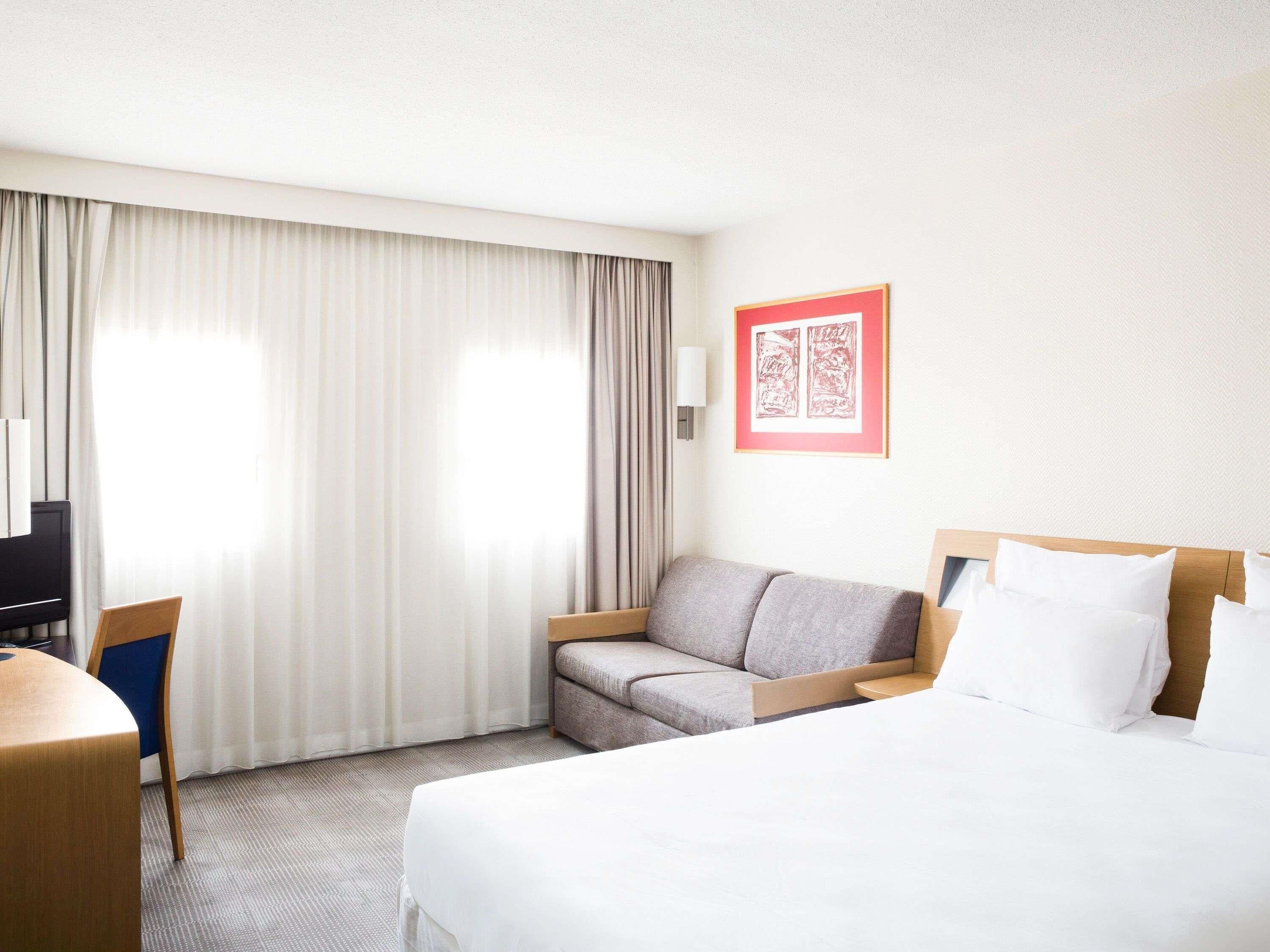 A hotel room with a bed, a sofa, a desk, and a TV.