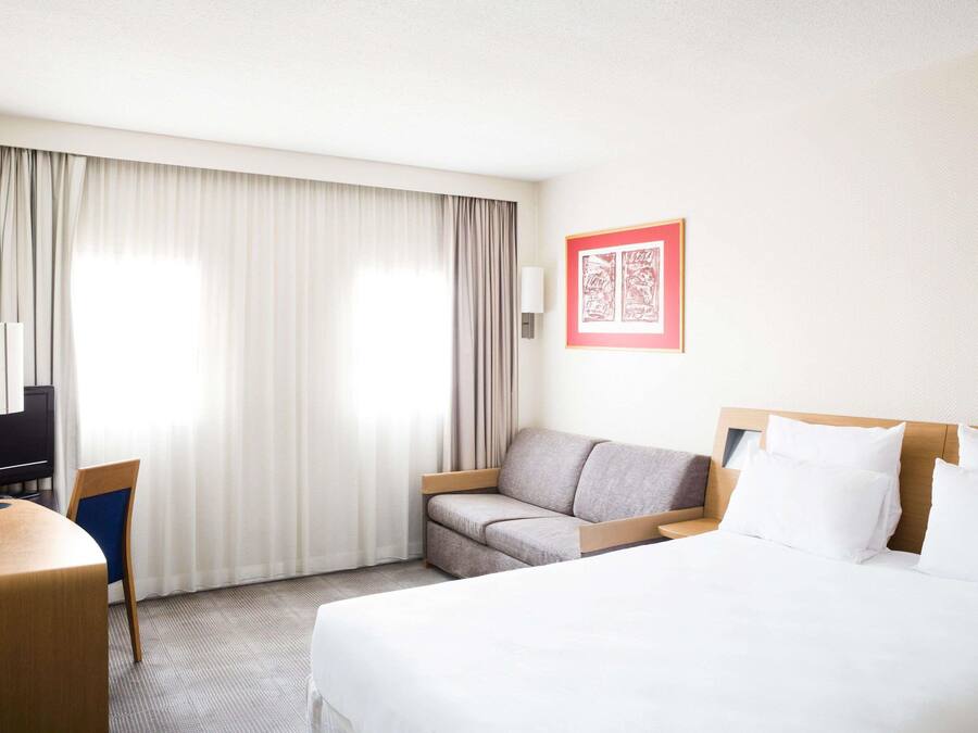 A hotel room with a bed, a sofa, a desk, and a TV.