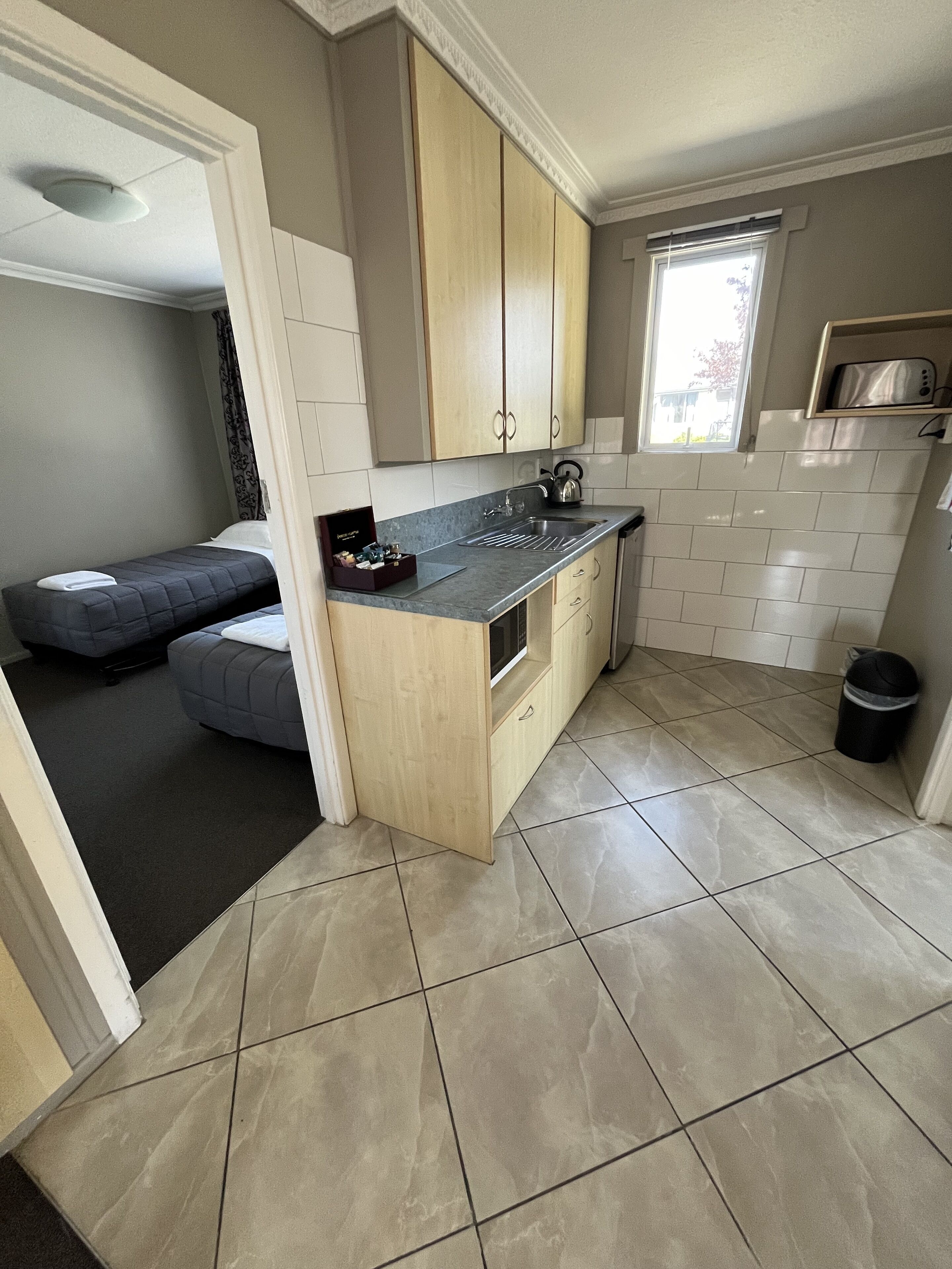 A compact kitchen with a built-in oven, a microwave, and a kettle. There is a small dining area with a bench and a window providing natural light.