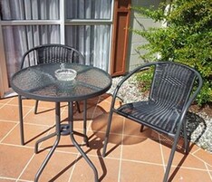 Un patio con una mesa redonda de vidrio y dos sillas de metal.