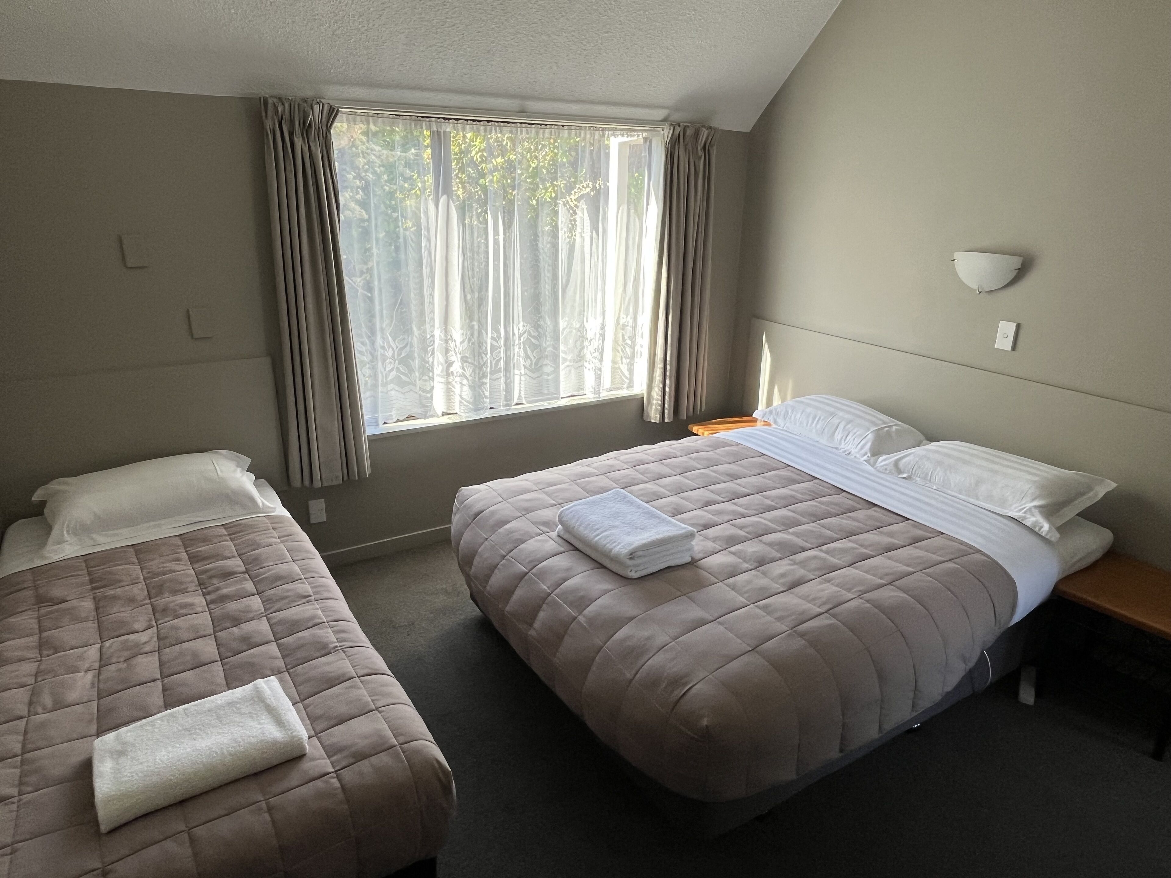 Hotelkamer met twee bedden, een raam met gordijnen, een nachtkastje en een wandlamp.