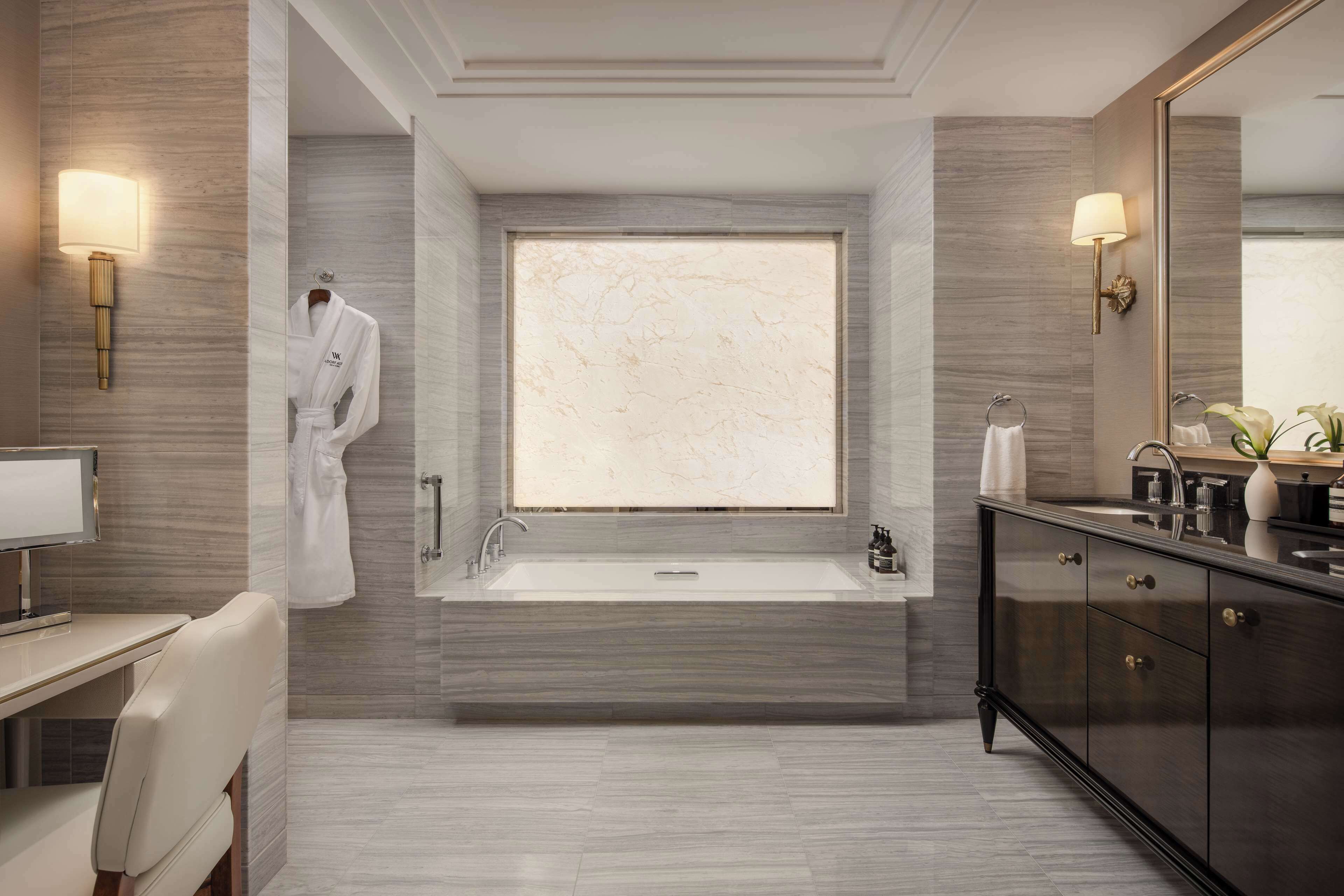 A modern bathroom with a large bathtub, a vanity with a mirror, and a robe hanging on the wall.