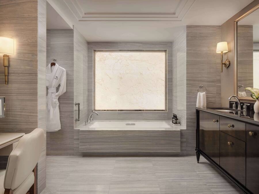 A modern bathroom with a large bathtub, a vanity with a mirror, and a robe hanging on the wall.