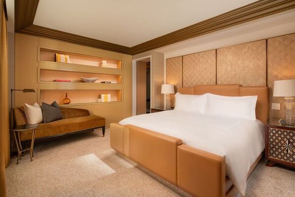 A hotel room with a large bed, a sofa, a side table, and a wall-mounted shelf with books and decorative items. - Waldorf Astoria New York (New York)
