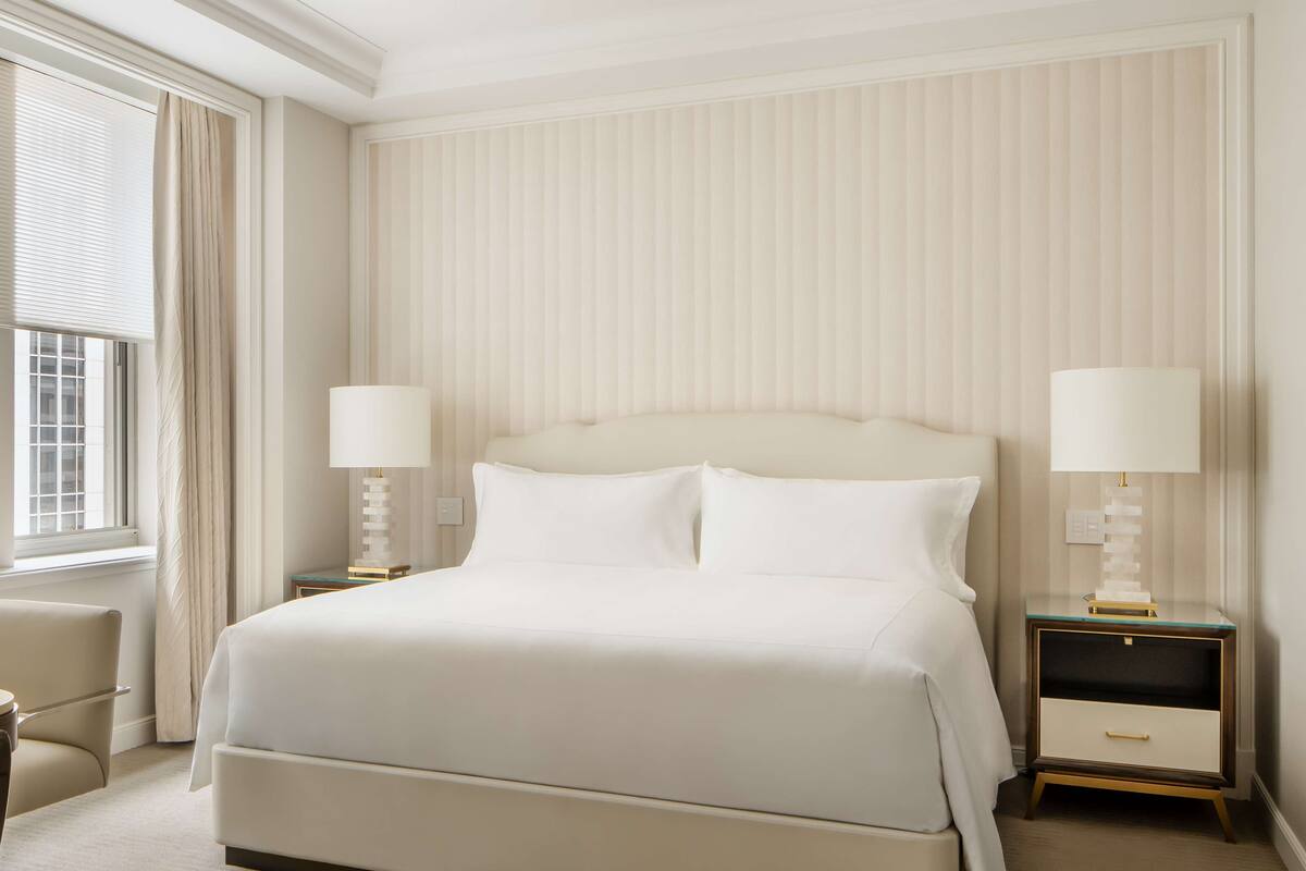 A hotel room with a large bed, two bedside tables with lamps, a chair, and a window with curtains.