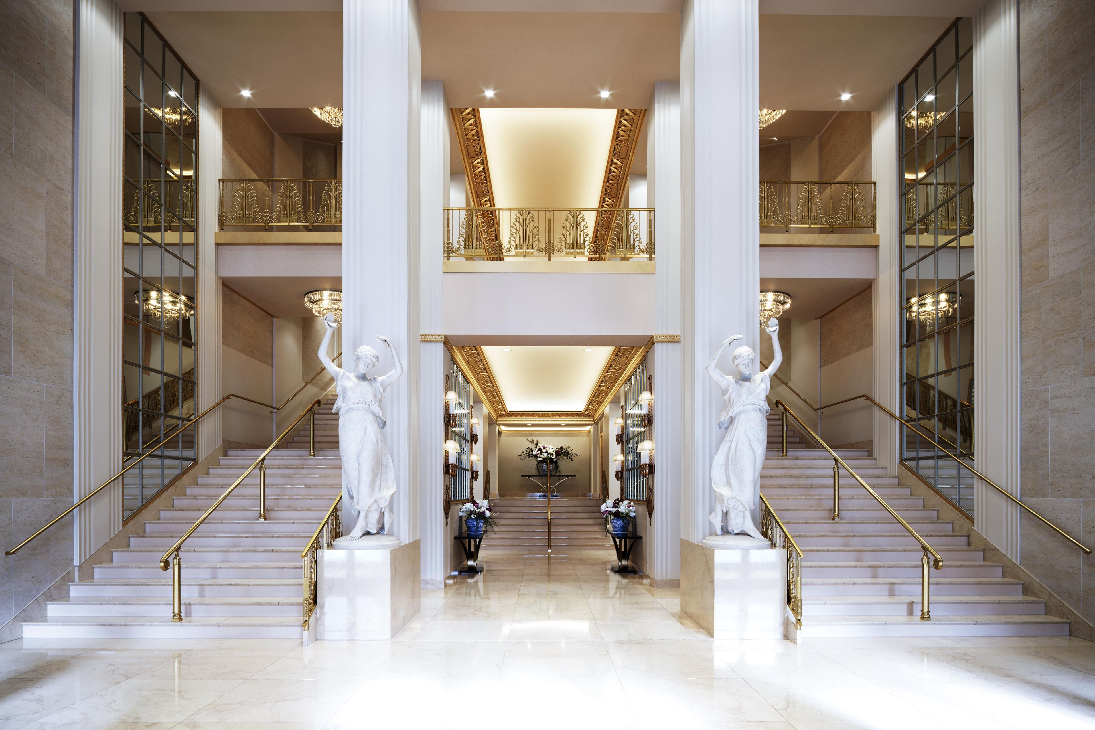A grand lobby with marble floors, double-height staircases, and ornate railings.