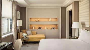 A hotel room with a bed, a sofa, a desk, and a small table with a lamp. There are wall-mounted shelves with decorative items.