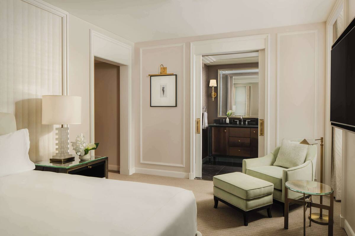 A hotel room with a bed, a nightstand with a lamp, a chair, a small table, and a mirror.