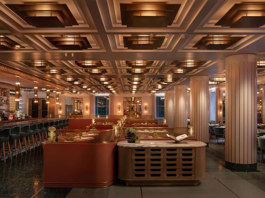 A spacious hotel lobby with a long bar area, seating arrangements, and a central decorative feature.