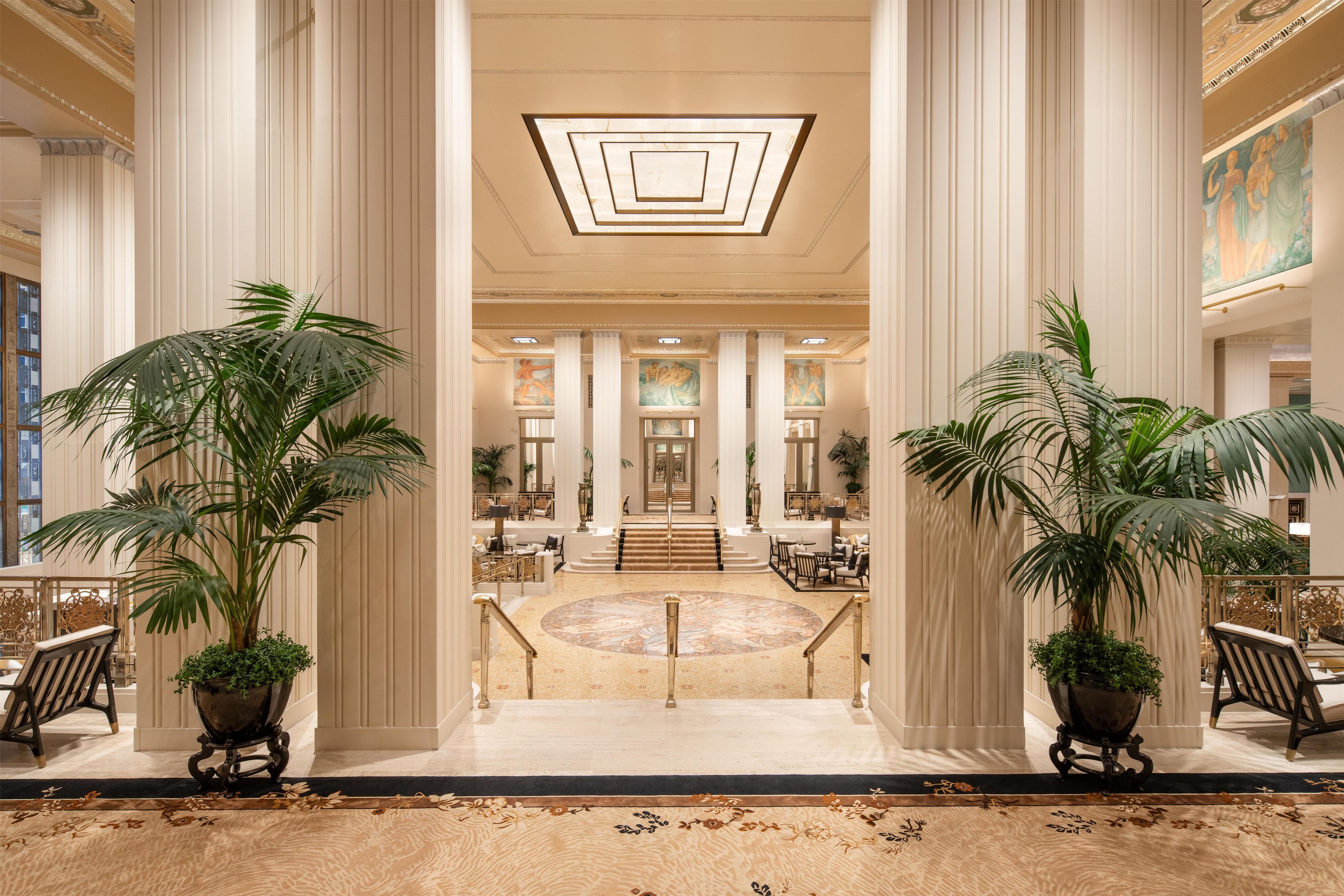 A grand lobby with high ceilings, large columns, and a central staircase leading to upper floors.