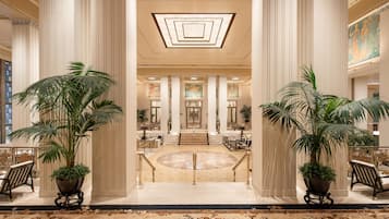 A grand lobby with high ceilings, large columns, and a central staircase leading to upper floors.