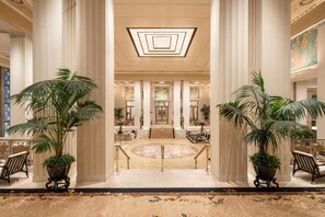 A grand lobby with high ceilings, large columns, and a central staircase leading to upper floors. - Waldorf Astoria New York (New York)