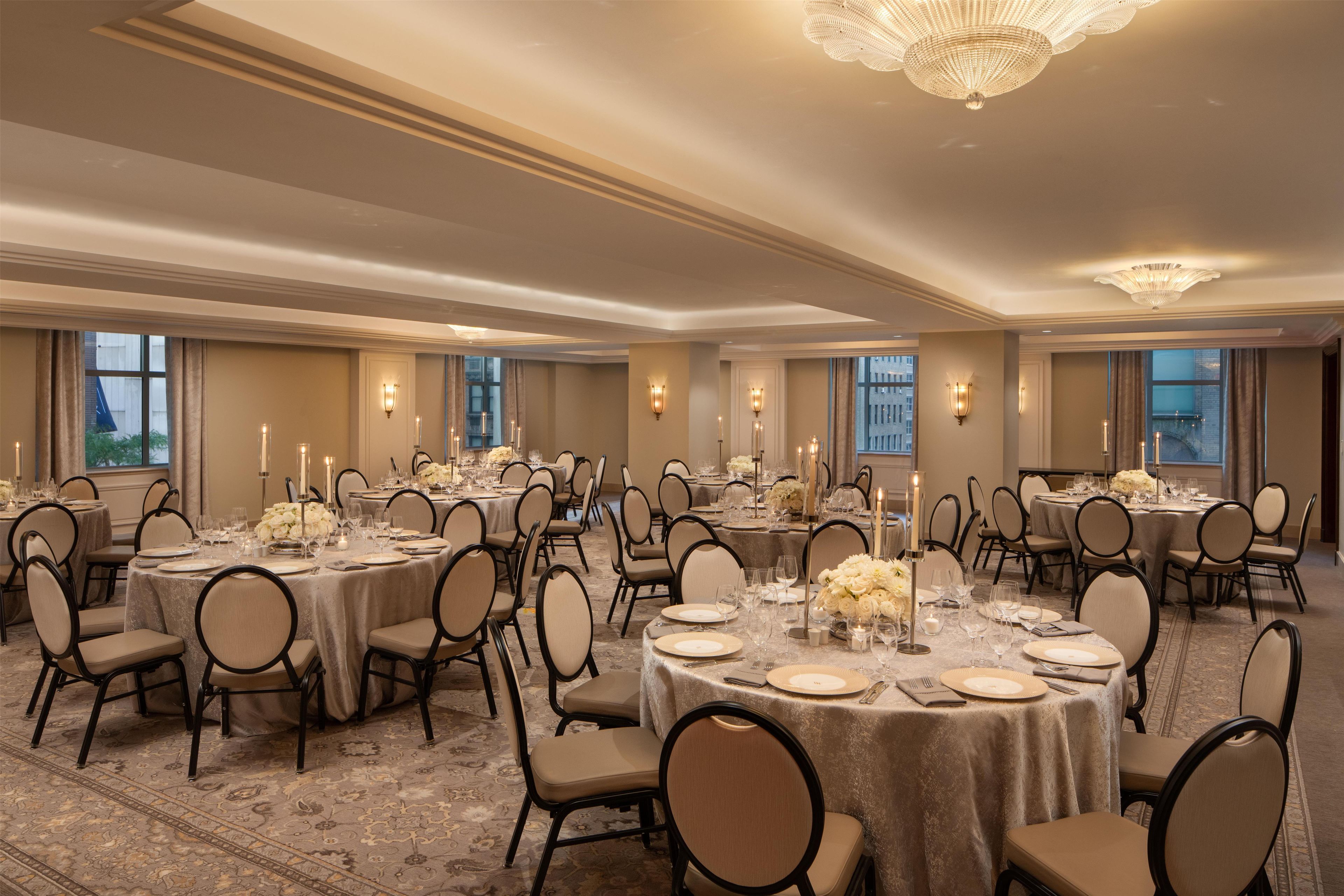A banquet hall with round tables set for dining, chairs, and candle centerpieces.