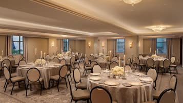 A banquet hall with round tables set for dining, chairs, and candle centerpieces.