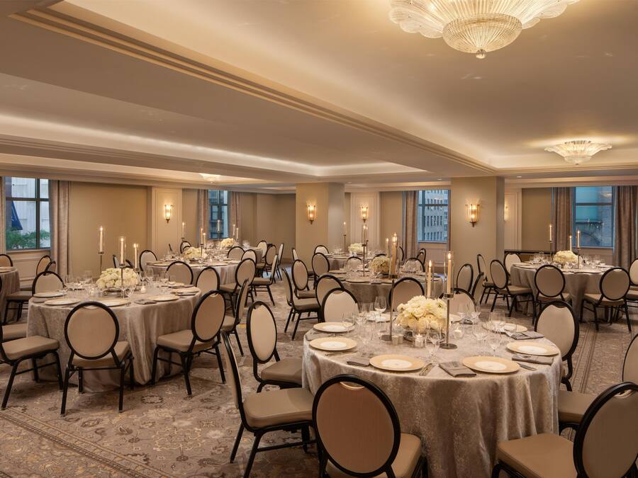 A banquet hall with round tables set for dining, chairs, and candle centerpieces.