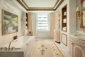 Une salle de bain luxueuse avec un lavabo en marbre, une grande baignoire et un tapis décoratif.