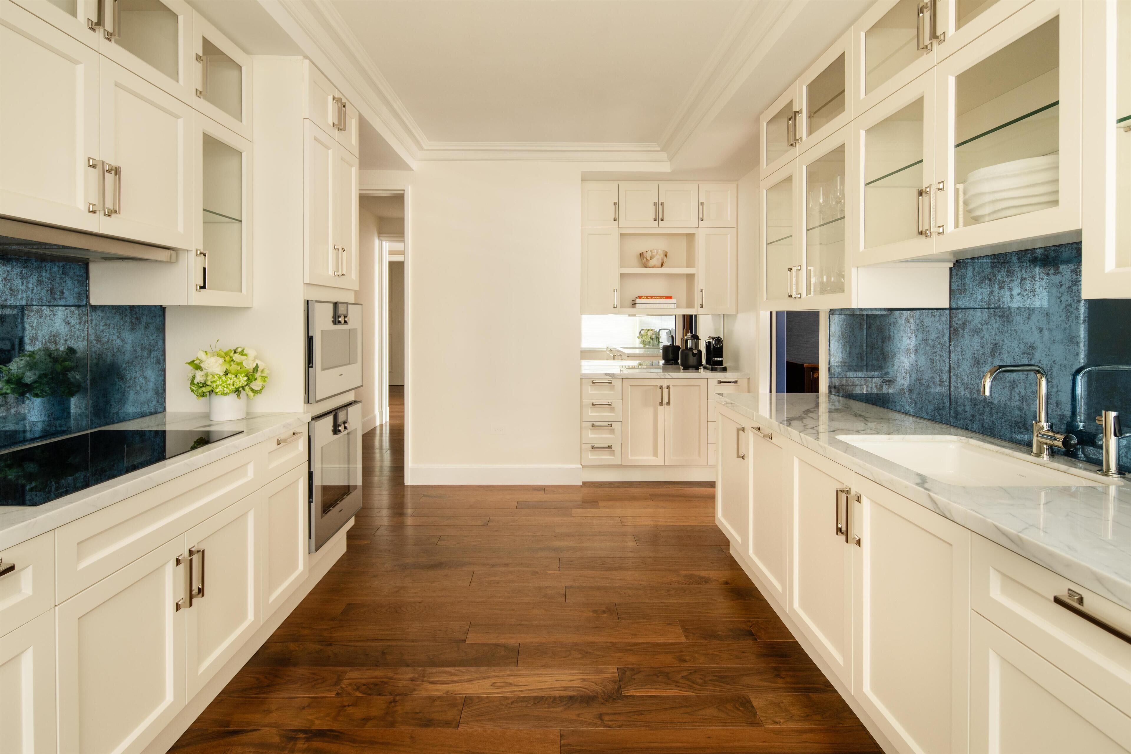 A modern kitchen with white cabinetry, a black backsplash, and a wooden floor.