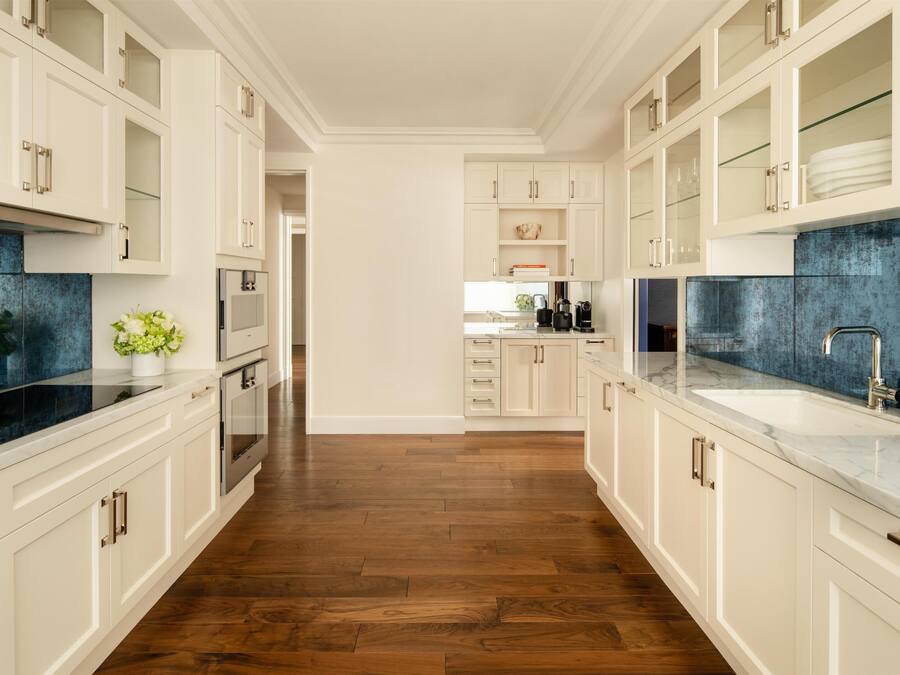 A modern kitchen with white cabinetry, a black backsplash, and a wooden floor.