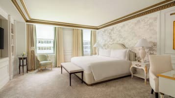 A hotel room with a large bed, a bedside table with a lamp, a chair, and a small table with a lamp.