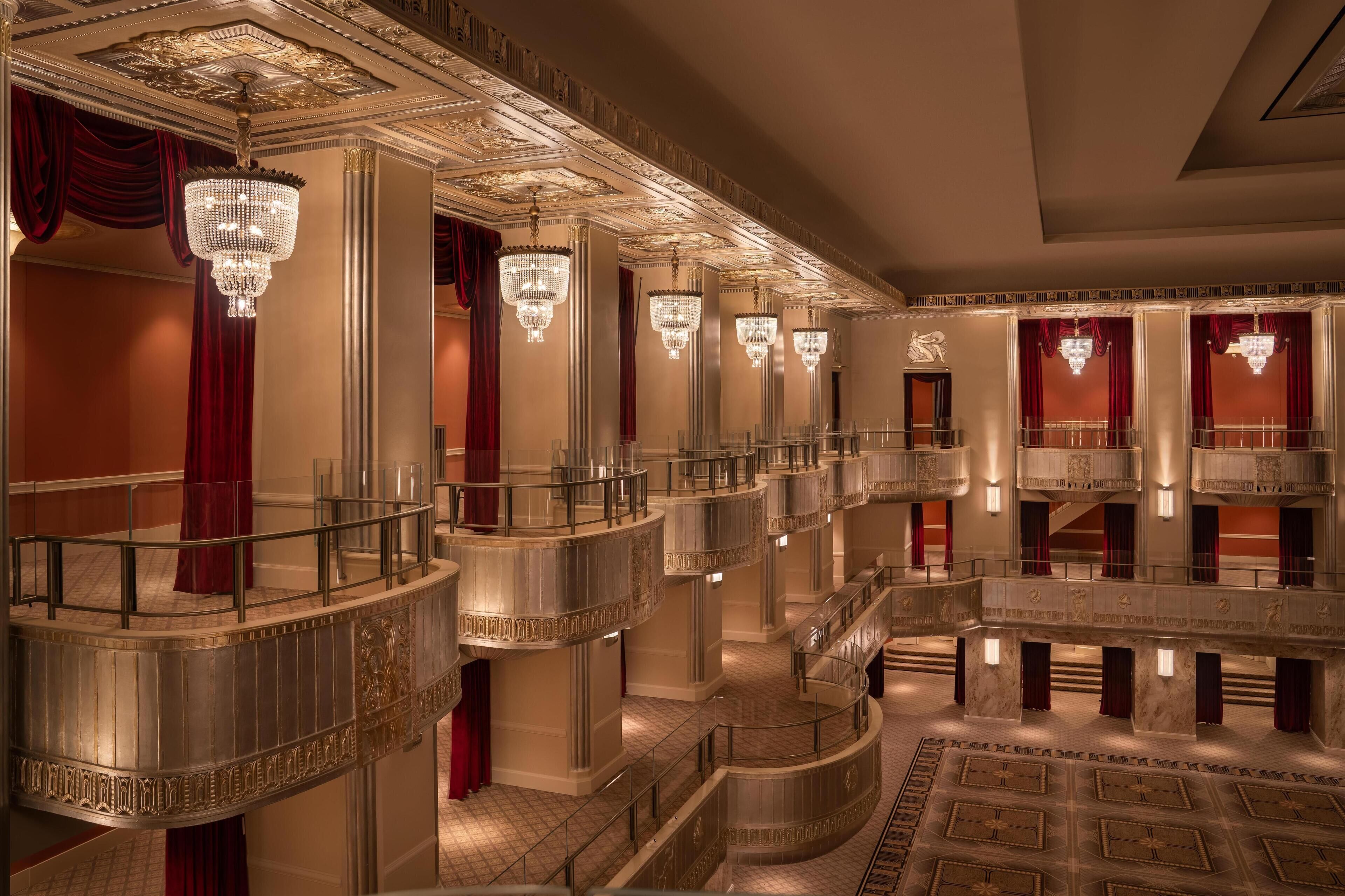 Um amplo hall de hotel com lustres requintados, colunas de mármore e um átrio espaçoso com uma escadaria central.