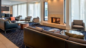 A modern hotel lobby with a fireplace, comfortable seating, and a large window offering a view. - Courtyard New Haven Wallingford (Wallingford)
