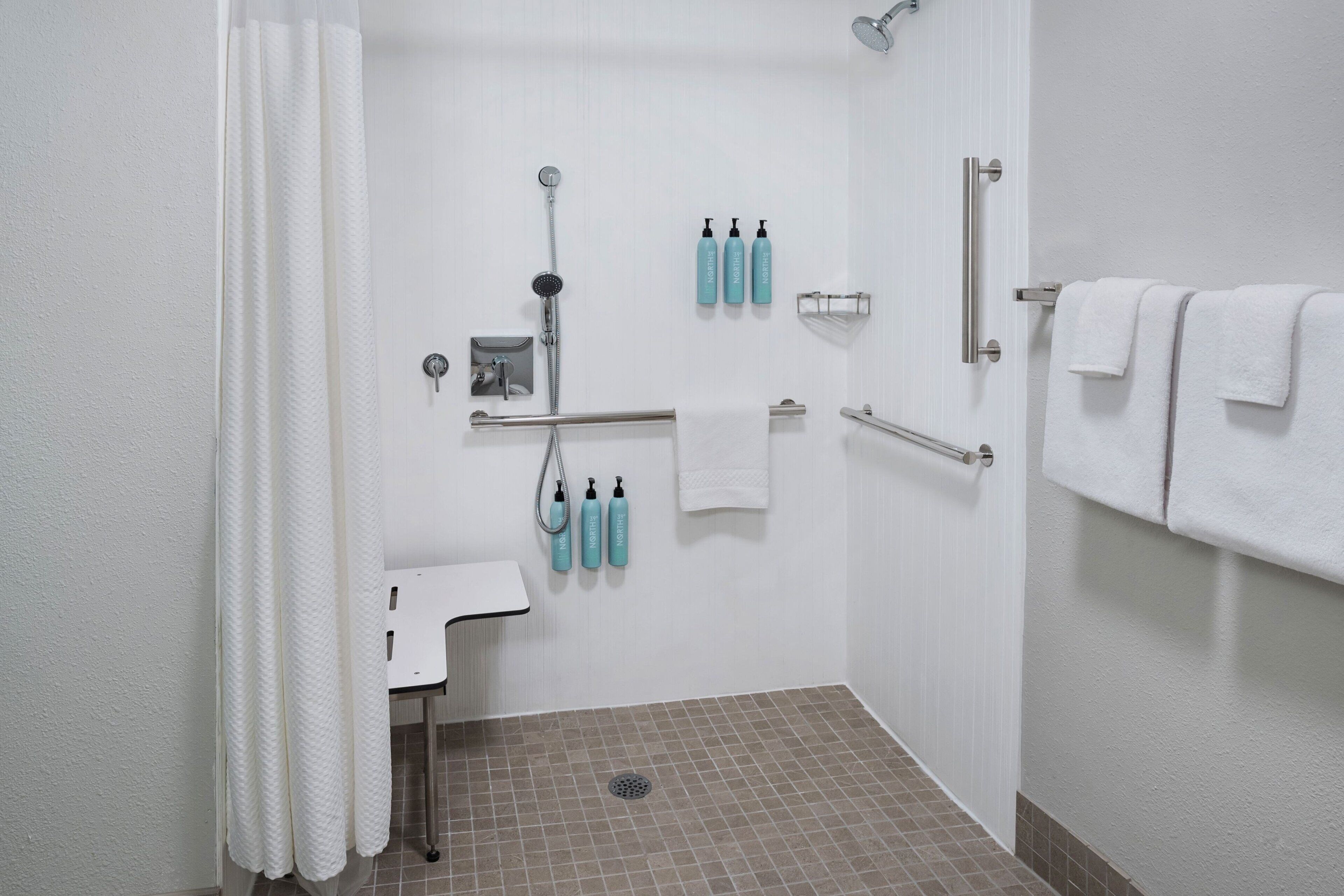 Un espace douche moderne équipé d’une barre d’appui, d’un lavabo blanc et d’un porte-serviettes.