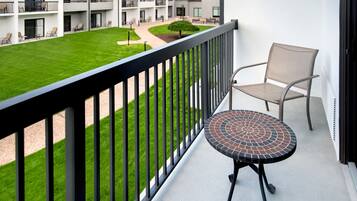 A balcony with a small table and a chair, overlooking a well-maintained lawn and a building with multiple balconies.
