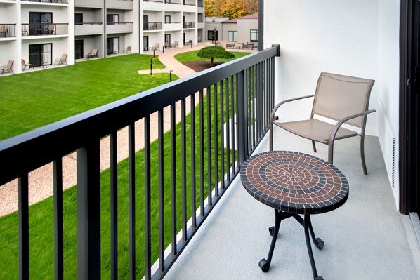 A balcony with a small table and a chair, overlooking a well-maintained lawn and a building with multiple balconies. - Courtyard New Haven Wallingford (Wallingford)