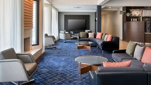 A modern hotel lobby with a large flat-screen TV, comfortable seating, a Starbucks coffee station, and a patterned carpet. - Courtyard New Haven Wallingford (Wallingford)