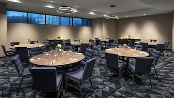 A conference room with round tables and chairs, large windows, and a carpeted floor.