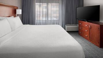 Habitación de hotel con una cama grande, televisión, cómoda de madera y una ventana con cortinas.
