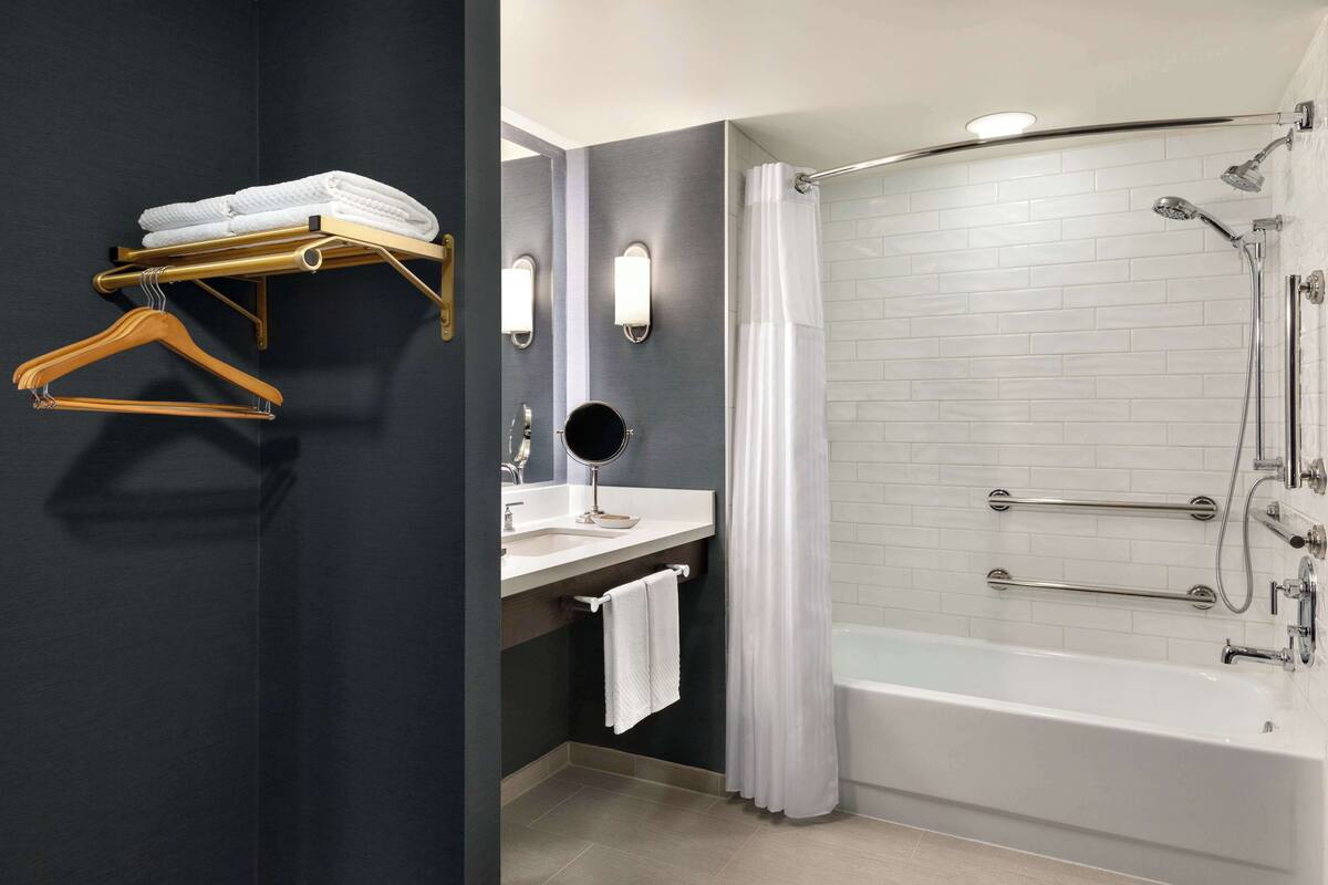 A modern bathroom with a bathtub, a vanity with a mirror, and towel racks.