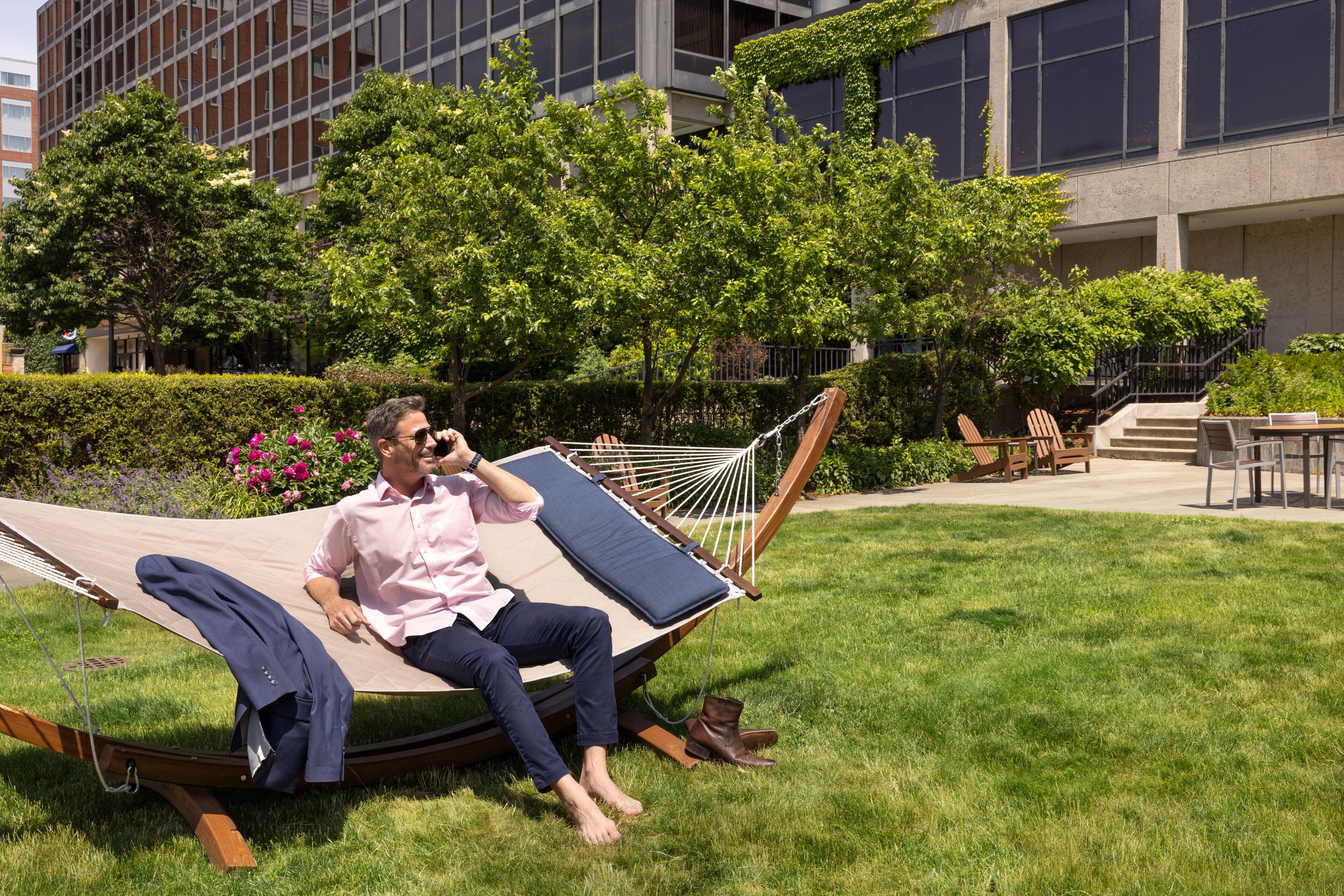 A man relaxing in a hammock on a grassy lawn with a building in the background.