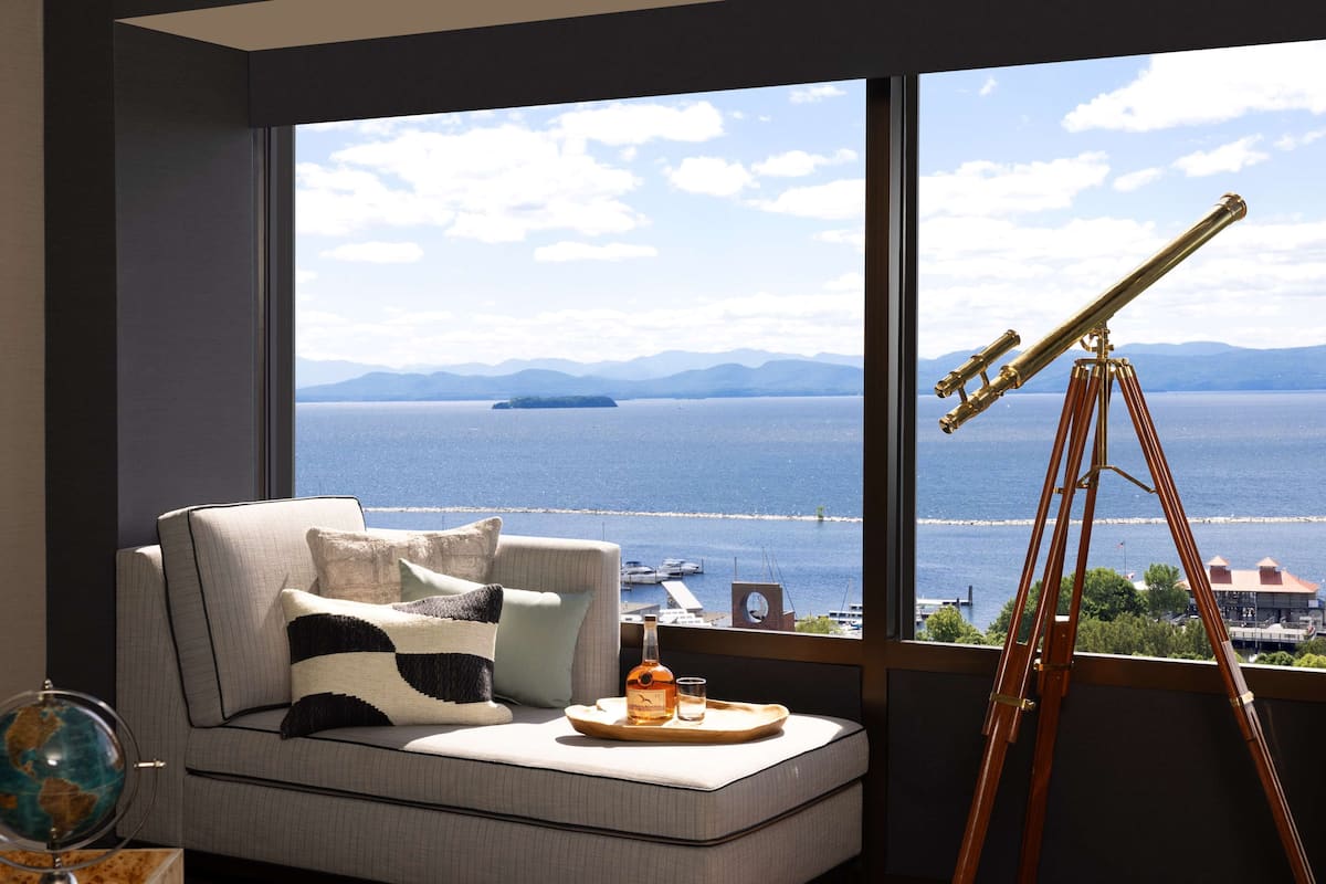 A room with a large window, a telescope, a sofa with cushions, a tray with a bottle and glass, and a globe on a side table.