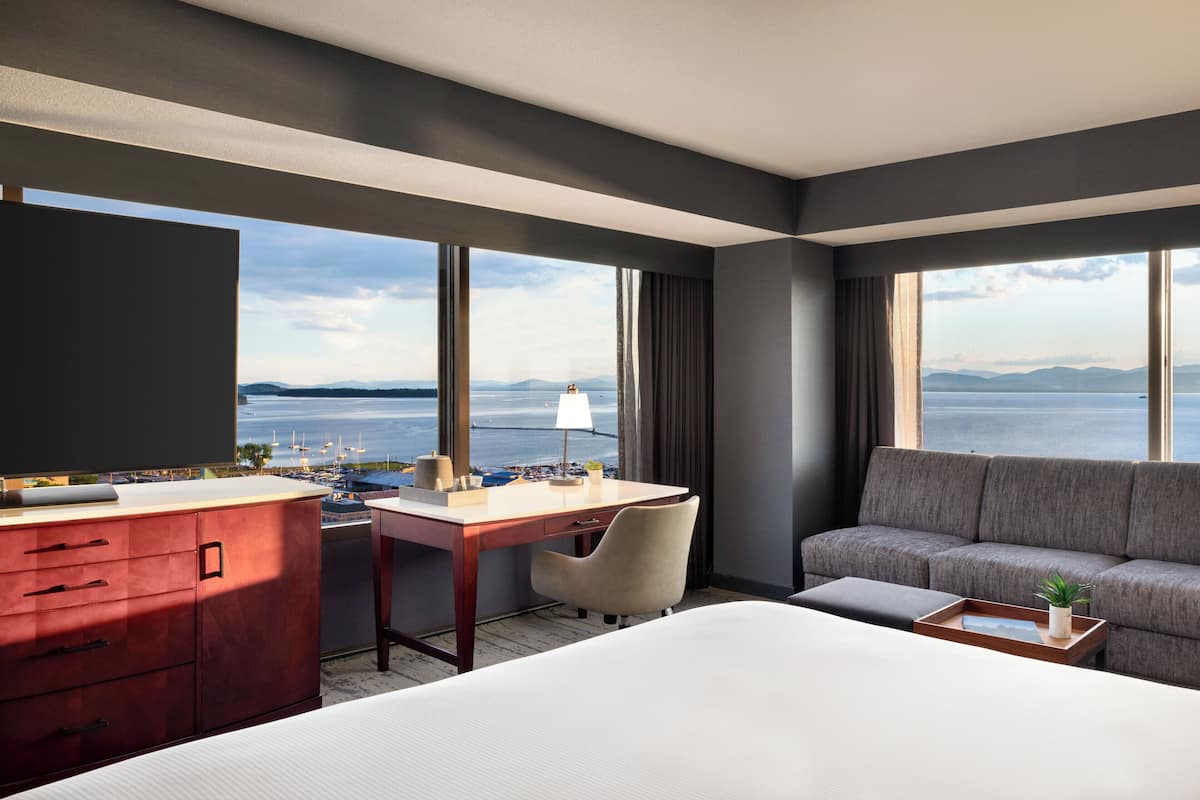A hotel room with a bed, a desk, a sofa, and a view of the sea.