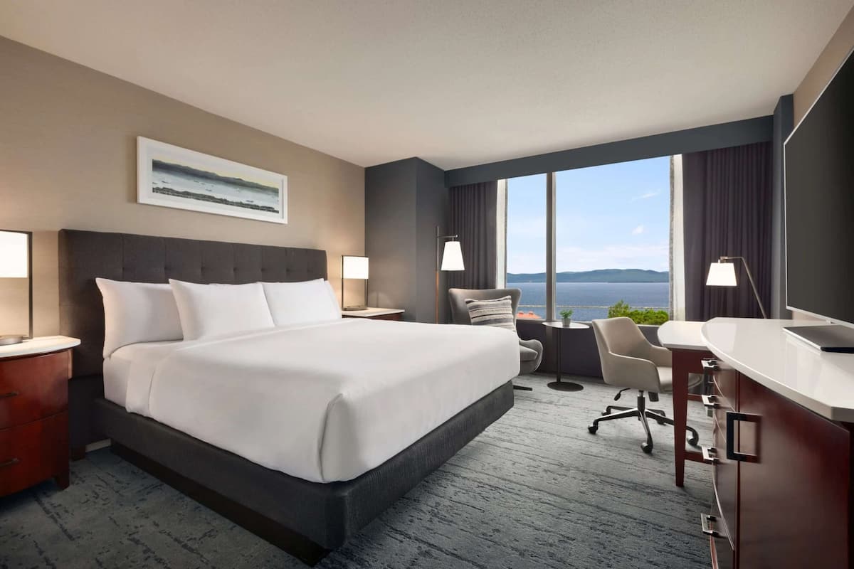A hotel room with a large bed, a desk, a chair, a TV, and a view of the sea.