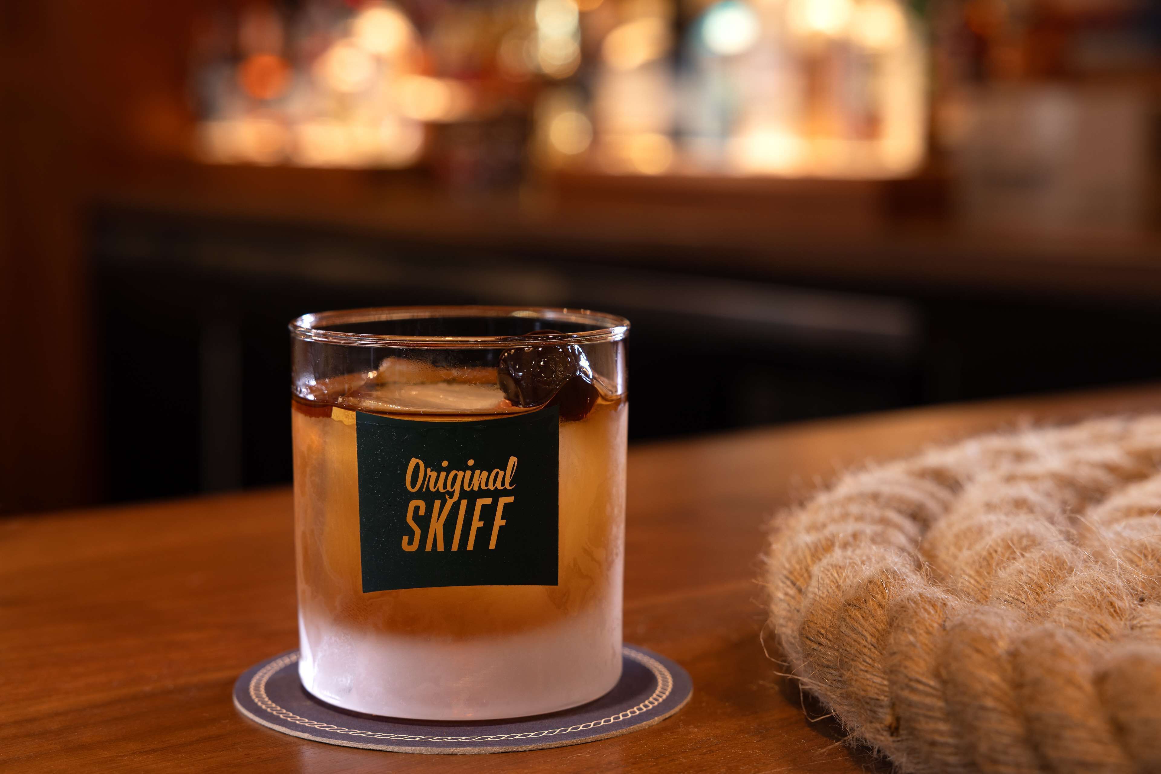 A candle labeled "Original SKIFF" on a wooden table with a coiled rope beside it.