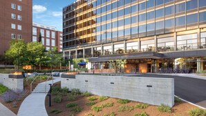 Un hotel moderno con fachada de vidrio, zona de estar exterior y jardín ajardinado.