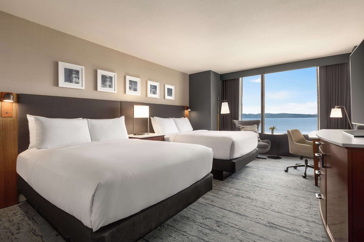 A hotel room with two beds, a desk, and a view of the sea.