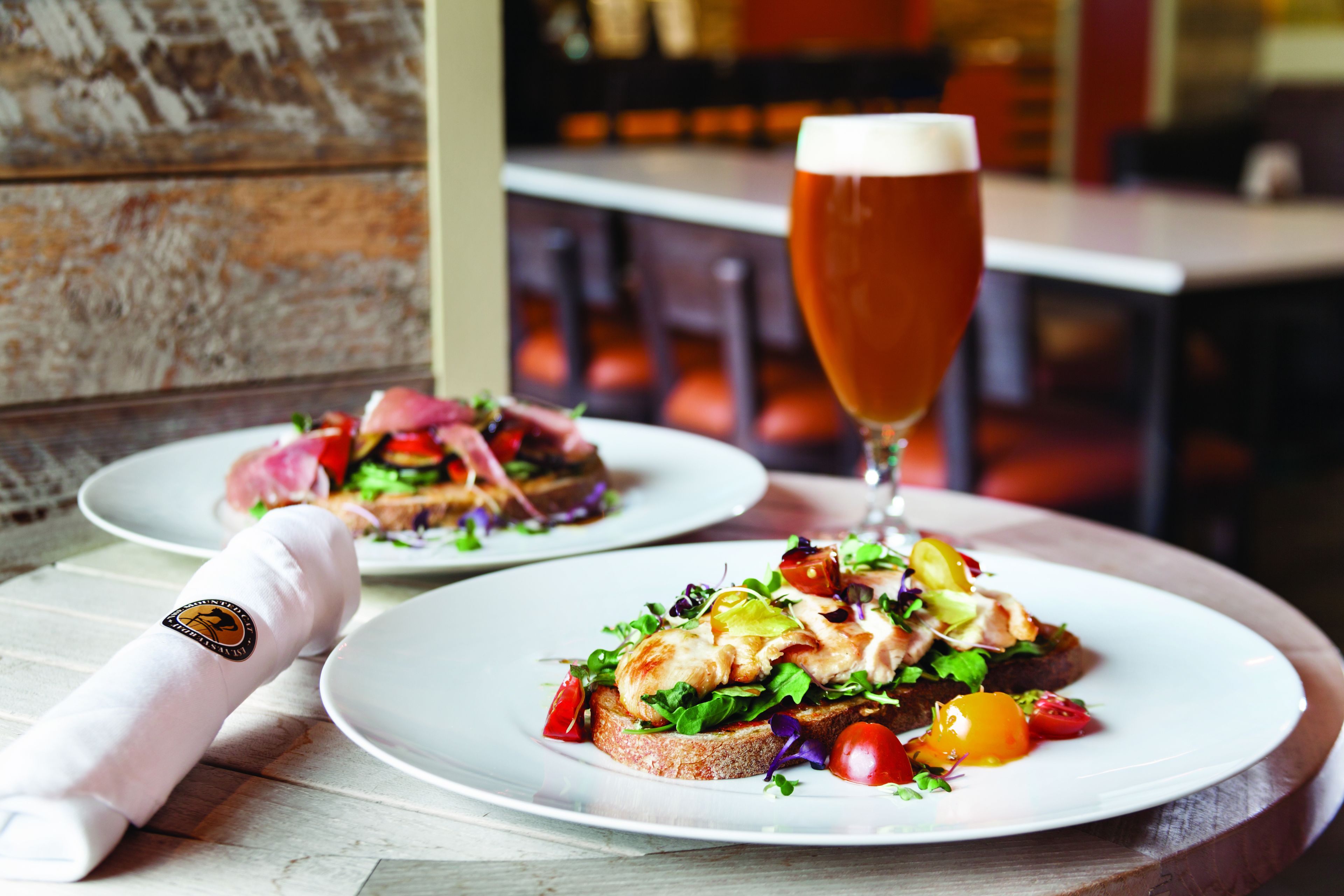 Two plates of food with a glass of beer on a wooden table in a restaurant.