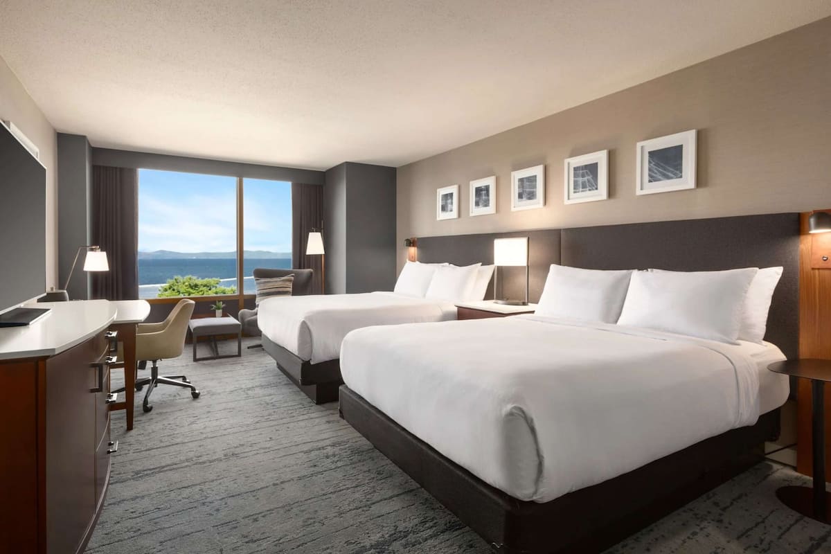 A hotel room with two beds, a desk, and a view of the ocean.