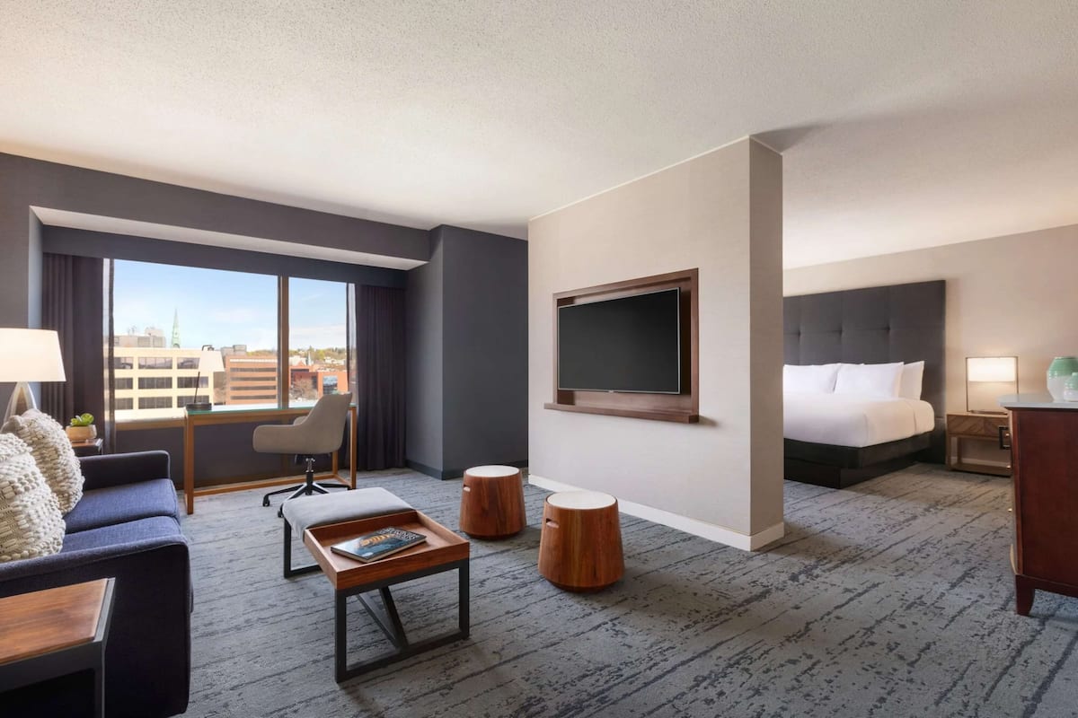 A hotel room with a large bed, a desk, a chair, a coffee table, and a TV.