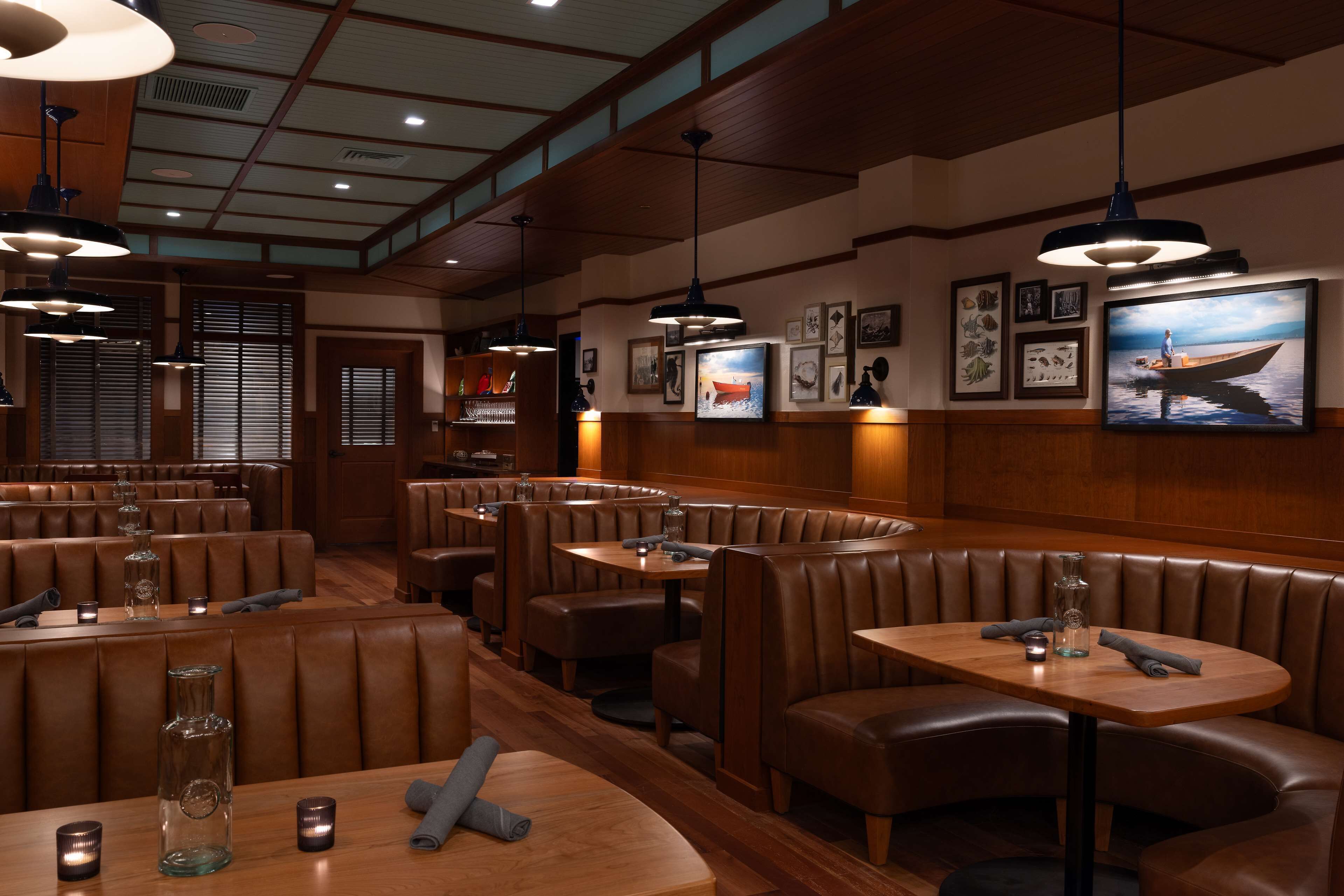 A restaurant with leather booths and tables, wooden ceiling, and framed pictures on the walls.