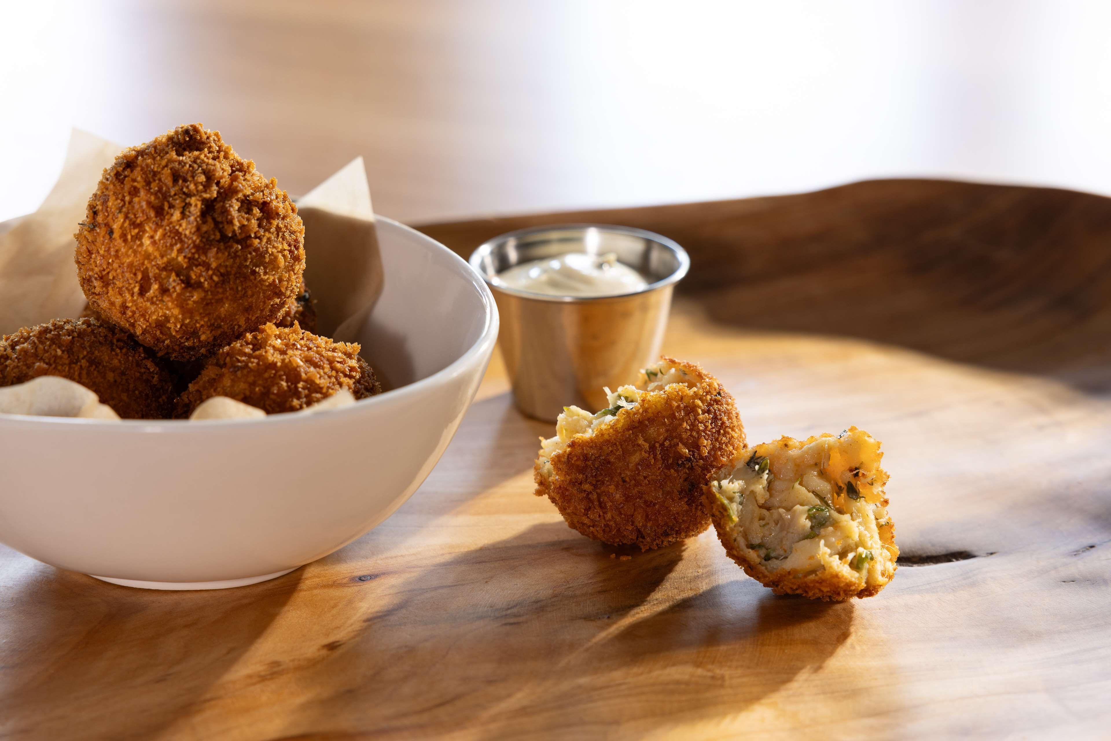 Un plato de comida frita, un trozo cortado y una pequeña taza de metal con salsa sobre una superficie de madera.
