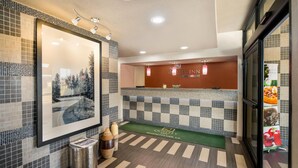 A hotel lobby with a reception desk, a framed picture on the wall, a green mat with the hotel logo, and a trash can. - Quality Inn near Parc Natchitoches (Natchitoches)
