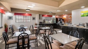 A modern hotel dining area with multiple tables and chairs, a kitchen in the background, and a ceiling with recessed lighting. - Quality Inn near Parc Natchitoches (Natchitoches)