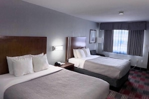 Quarto de hotel com duas camas, uma mesa de cabeceira, um abajur, uma janela com cortinas e piso coberto por carpete.