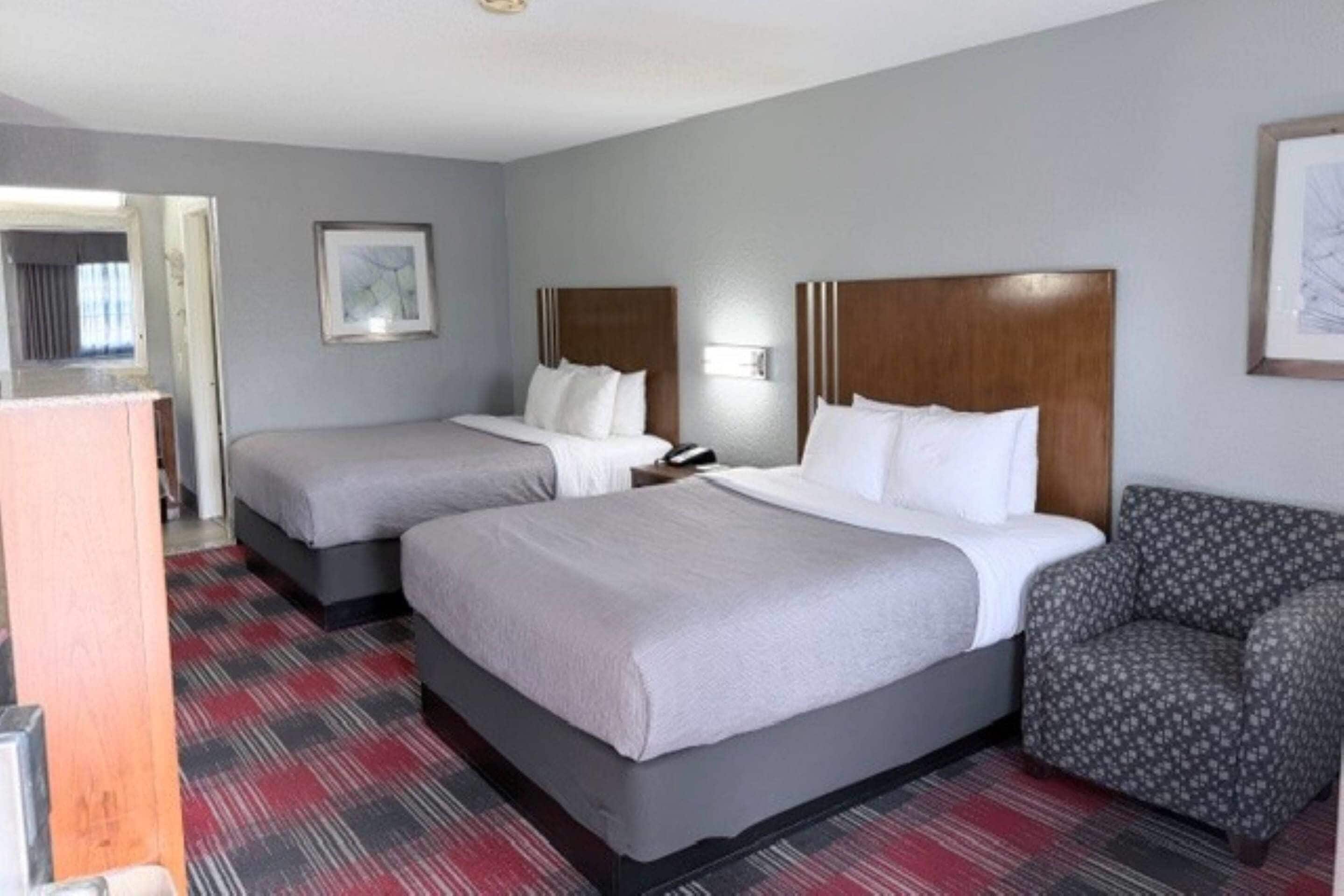 A hotel room with two beds, a chair, a desk, and a framed picture on the wall.